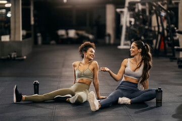 Two fit female friends taking a break and chatting in a gym.