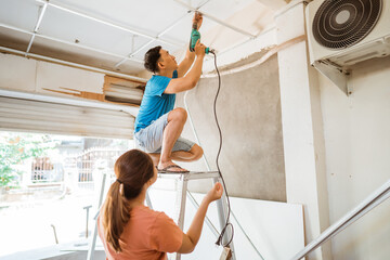 husband and wife work together to install a ceiling frame using a drill during home renovations