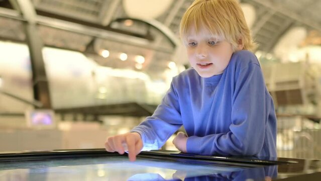 A child of primary school age visiting a science museum. The boy is exploring information about the exhibition exhibits on an interactive touch screen display
