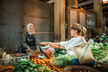 Fototapeta premium greengrocery seller helping customer picking vegetables from her stall in the farmer market