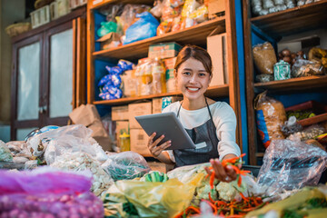 happy female vegetable seller checking products using tablet
