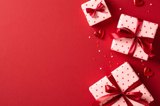 St Valentine's Day background. Flat lay composition with pink gift boxes wrapped red ribbon bows, red hearts, confetti on red table.