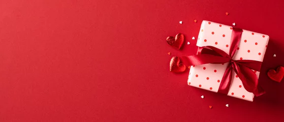 Fotobehang Pink gift box wrapped red ribbon bow with red hearts and confetti on red background. Happy St Valentines Day, Mothers Day, birthday concept. © photoguns