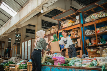 female asian green grocery seller giving customer vegetables in paperbag