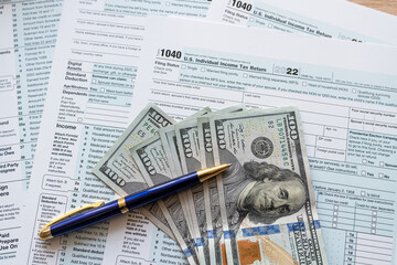 1040 tax form with pen and us dollar bills on desk