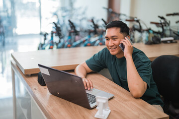 male business owner uses cell phone while working on laptop computer in store