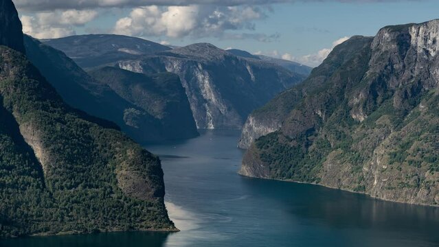Breathtaking view of the Aurlandsfjord. Forest-covered mountains rise from the dark waters. White clouds whirl above. A timelapse video.