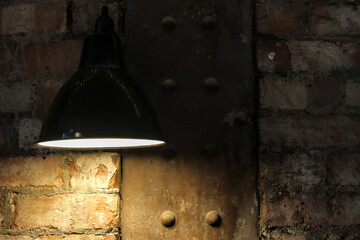 Pendant light partially illuminating an old brick wall and a riveted metal beam.