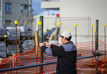 A worker installing the orange safety barrier mesh at a construction site