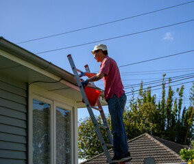 Man standing on the ladder and cleaning the gutter. Home maintenance work. Auckland.