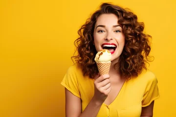 Poster Young woman eat ice cream with chocolate glaze on yellow background © Iryna