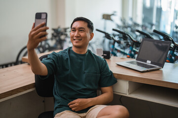 young man taking a selfie with his cell phone while working at his desk - obrazy, fototapety, plakaty