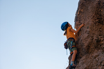 climber boy. the child trains in rock climbing. cute teen kid climbing on rock with insurance,...