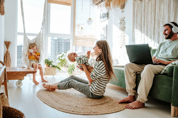 Mother playing with her son in living room at home with father using laptop