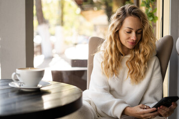 Beautiful blonde woman drinking coffee in cafe using smartphone, shopping online