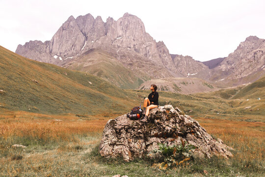 Woman sitting with backpack on rock in front of mount Kazbek