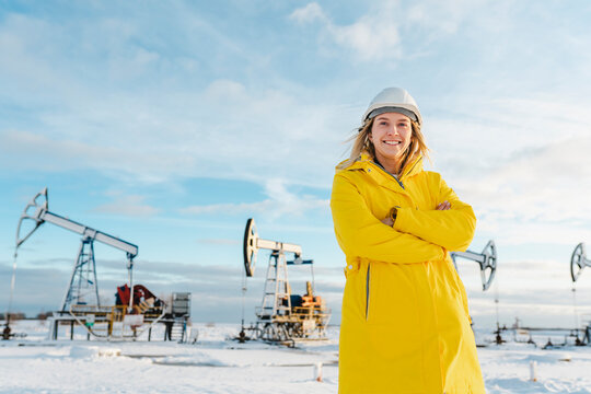 Smiling young engineer with arms crossed standing at oil production field in winter