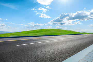 Asphalt road and green meadow with mountain nature landscape under blue sky - obrazy, fototapety, plakaty