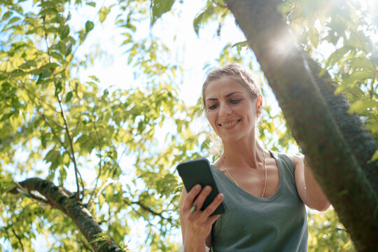 Smiling woman using smart phone standing by tree