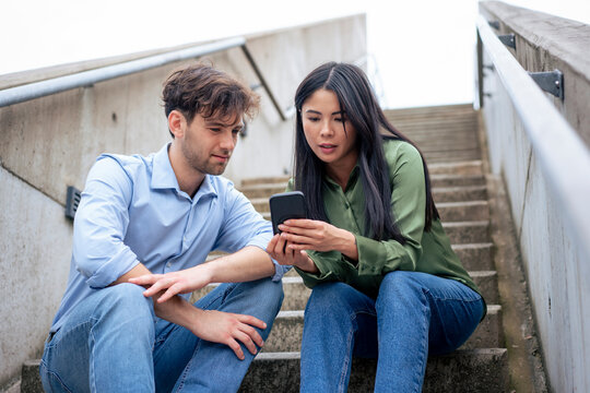 Woman sharing smart phone with friend sitting on steps