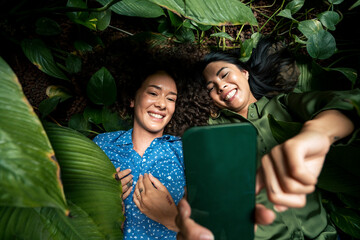 Smiling woman taking selfie on smart phone with friend lying amdist plants
