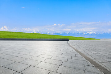 Empty square floor and green grass with snow mountain natural landscape under blue sky
