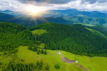 Scenic aerial view of the foggy Carpathian mountains, village and blue sky with sun and clouds in morning light, summer rural landscape