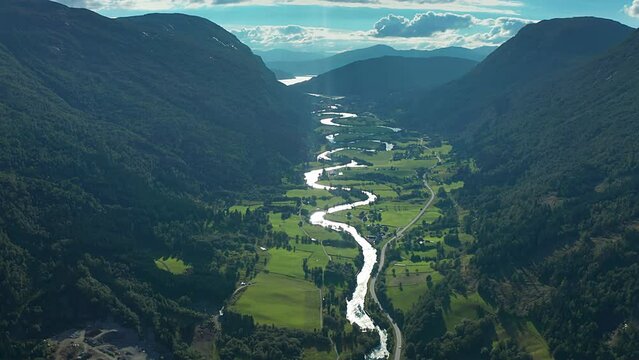 Flight over the Stryneelva river with its' many turns winds through the lush green Strynedalen valley in Norway. A narrow road follows the river. Aerial view.