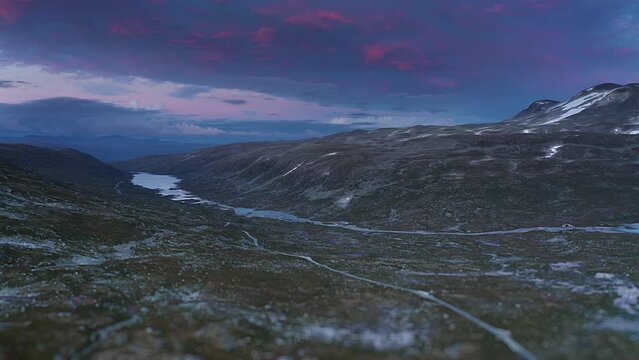 Ascent over the Gamle Strynefjellsvegen with a magnificent blue and red sunset in the background . An old road crosses a mountainous plateau.