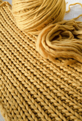 Fototapeta na wymiar Handmade yellow yarn scarf. A ball of thread and a yellow scarf are on the table.