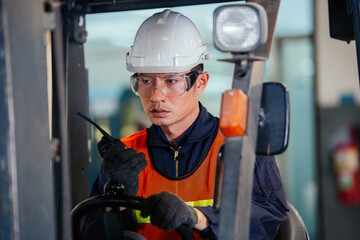 Asian male warehouse worker talking on radio phone or walkie-talkie with colleague driving forklift car in heavy industry manufacturing factory. portrait of men working hard. shipping delivery product