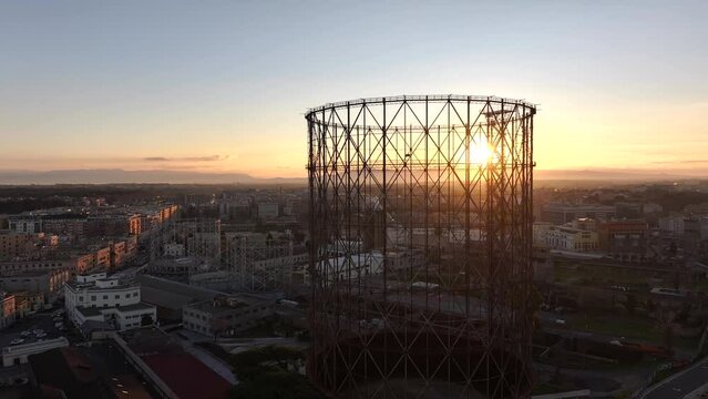 Alba sul Gazometro del quartiere post industriale Ostiense a Roma, Italia.
Veduta aerea con drone dei raggi del sole che passano attraverso la vecchia struttura del Gasometro.