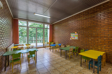 Kindergarten dining room with brick walls, large window and colorful furniture.