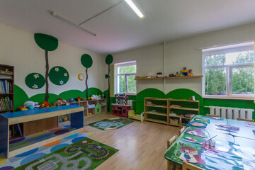 A kindergarten playroom with drawings on the walls and lockers with books and toys.