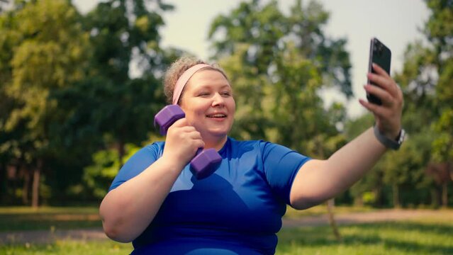 Funny overweight woman posing for selfie with dumbbell in hand, active lifestyle