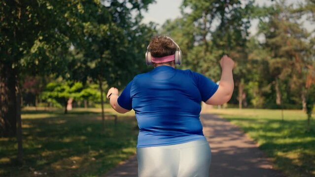 Funny active plus size woman dancing during outdoor workout, wearing earphones