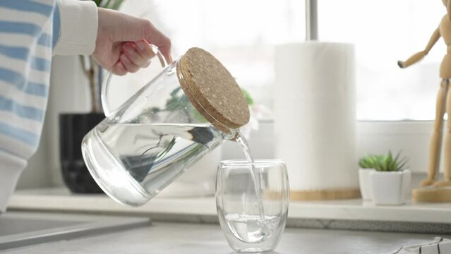 Woman pouring fresh pure water from jug into glass in kitchen, Quenching thirst, Lifestyle healthcare concept