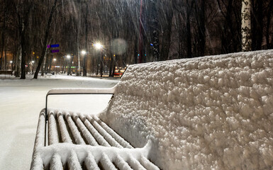Benches under the snow in the park on a winter evening.