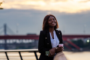 In a tranquil moment, the businesswoman of color leans against the railing, savoring the river's...