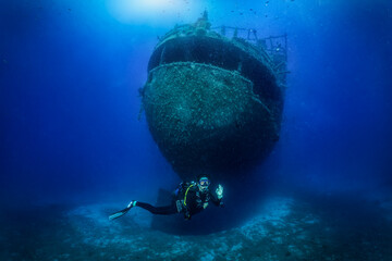 A female scuba diver explores a large shipwreck on the seabed of the Aegean Sea, Naxos island, Greece - obrazy, fototapety, plakaty