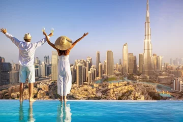 Crédence de cuisine en verre imprimé Dubai A happy tourist couple on vacation time stands by the pool edge and enjoys the panoramic sunset view of the Dubai city skyline, UAE