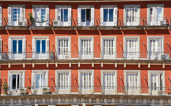 Front view of a colorful orange facade with white doors or jalousies. Balconies with white shutters or blinds on an orange exterior. Latin or Spanish architecture in Plaza Mayor - Madrid, Spain