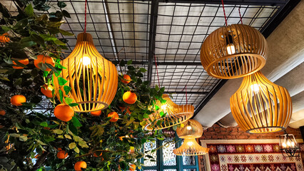 Yellow wicker chandeliers on the ceiling and orange tree with tangerines. Interior, room design,...