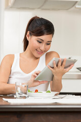 Young Asian woman eating and reading a tablet PC.