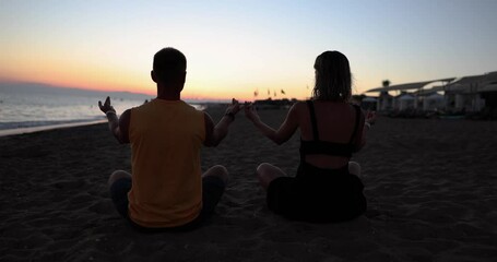 Couple yoga for meditation and meditating at serene sunset on beach. Girl and man are relaxing in lotus position in calm zen moment