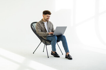 Young smiling businessman sitting in office chair and working on laptop on white background
