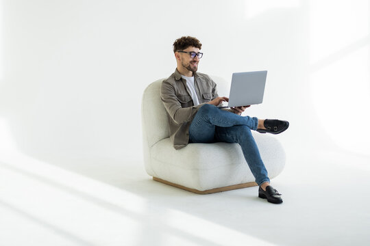 Portrait of attractive man sitting in chair using laptop calling contact over white background