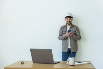 Young man smiling and using cellphone while sitting on desk in office indoors