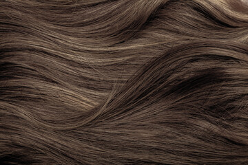 Brown hair close-up as a background. Women's long brown hair. Beautifully styled wavy shiny curls....