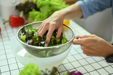 Senior man washing the vegetables from the garden while making healthy salad in kitchen.